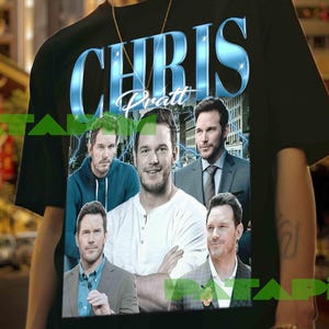 Peut inclure: T-shirt noir avec le nom "CHRIS Pratt" dans une police bleue stylisée. Le t-shirt présente plusieurs images de Chris Pratt. L'arrière-plan montre une rue de la ville avec des bâtiments et des lumières.