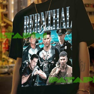 Op de afbeelding: Zwart t-shirt met een afbeelding van Jon Bernthal en de tekst "BERNTHAL Jon" in een zilveren, chroomachtige letter. De afbeelding bevat afbeeldingen van Bernthal in verschillende rollen. Het t-shirt wordt door een persoon gedragen.