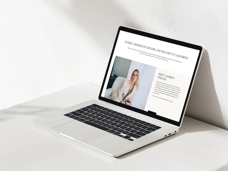 Op de afbeelding: Een zilveren laptop die een webpagina toont met de titel AUDREY I REPRESENT BUYERS AND SELLERS IN CALIFORNIA. Het scherm toont een foto van een persoon in een beige blazer en tekst over Audrey Wilson, een vastgoedprofessional.