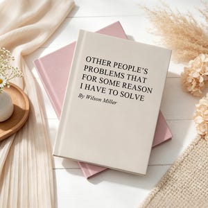 May include: A hardback book with a cream-coloured cover featuring the black printed text "OTHER PEOPLE'S PROBLEMS THAT FOR SOME REASON I HAVE TO SOLVE By Wilson Miller" resting on top of a pink book, positioned on a white wooden surface.