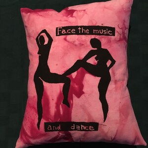 May include: Pink decorative pillow with black silhouettes of two dancers. The pillow has the text "Face the music" and "and dance" in black. The pillow has a tie-dye effect.