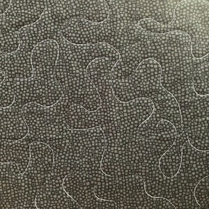 May include: Close-up of a quilted fabric with a dark gray background featuring a pattern of small squares. White thread creates a flowing, organic design across the surface. The quilting adds texture and visual interest to the textile.