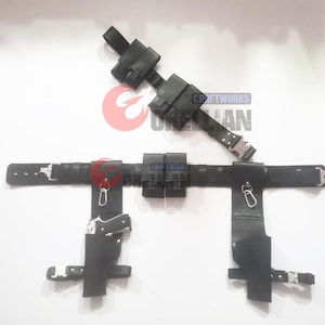 Puede incluir: Cintur&oacute;n utilitario de cuero negro con m&uacute;ltiples bolsas, fundas y una hebilla. El cintur&oacute;n incluye una funda para una pistola y est&aacute; dise&ntilde;ado con una est&eacute;tica t&aacute;ctica. El texto "CRAFTWORKS ORELLAN" es visible en el cintur&oacute;n.