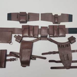 Op de afbeelding: Een bruin utility-riemsysteem met meerdere modulaire tasjes, holsters en riemen. De set bevat een hoofdriem met diverse rechthoekige tasjes, twee beenholsters met verstelbare gespriemen en extra accessoiretasjes met klittenbandsluitingen.