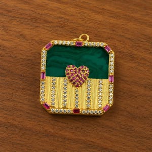 May include: A gold-colored pendant with a rectangular shape, featuring a green malachite center and a heart-shaped cluster of pink gemstones. The pendant is adorned with white and pink gemstones around the edges.