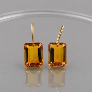 以下が含まれることがあります： エメラルドカットが施された長方形のシトリン宝石を使用したゴールドのドロップピアス一対。それぞれのピアスには、鮮やかな半透明のオレンジイエローの石の上部中央に、磨き上げられたゴールドのフックワイヤーが取り付けられており、シンプルで洗練されたデザインとなっています。