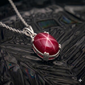 May include: A silver necklace featuring a large, oval, deep red gemstone pendant. The gemstone has a star-like pattern across its surface. The pendant is set in a silver bezel and hangs from a delicate silver chain.