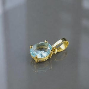 Peut inclure: Un pendentif en or avec une pierre précieuse bleu clair de forme ovale à facettes, maintenue par quatre griffes. Le pendentif comprend une bélière en or poli sur le dessus pour l'attacher à une chaîne, avec une finition métallique brillante.