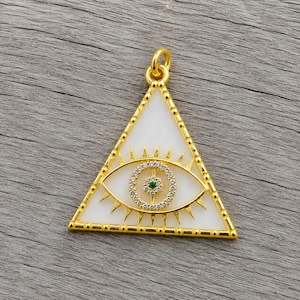 Op de afbeelding: Goudkleurige hanger in de vorm van een driehoek met een witte achtergrond. De hanger heeft een oogontwerp met een groen centrum en een cirkel van heldere stenen. Het oog is omgeven door gouden stralen.