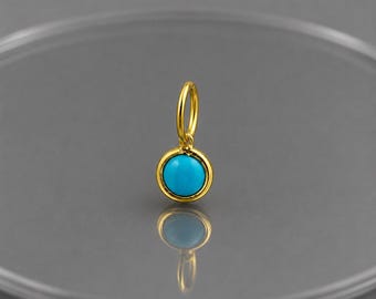 May include: A small, round gold charm featuring a smooth, bright turquoise cabochon stone set in a polished gold bezel. The charm includes a circular gold jump ring at the top, designed for attachment to a necklace chain or a bracelet link.