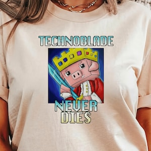 May include: Cream-colored t-shirt featuring a cartoon pig wearing a crown and holding a sword. The text "TECHNOBLADE NEVER DIES" is printed above and below the pig illustration in a gradient font.
