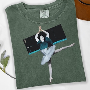May include: Green Comfort Colors t-shirt featuring a ballet dancer image. The dancer is wearing a white tutu and a dark green cape. The shirt has a classic crew neck and the Comfort Colors tag is visible.