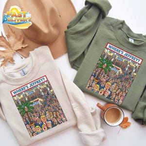 May include: Two sweatshirts, one cream and one olive green, each with a graphic that says "WHERE'S JEFFREY?" in a red box. The graphic is a cartoon scene with many people and a palm tree. A brown hat and a cup of coffee are also in the image.