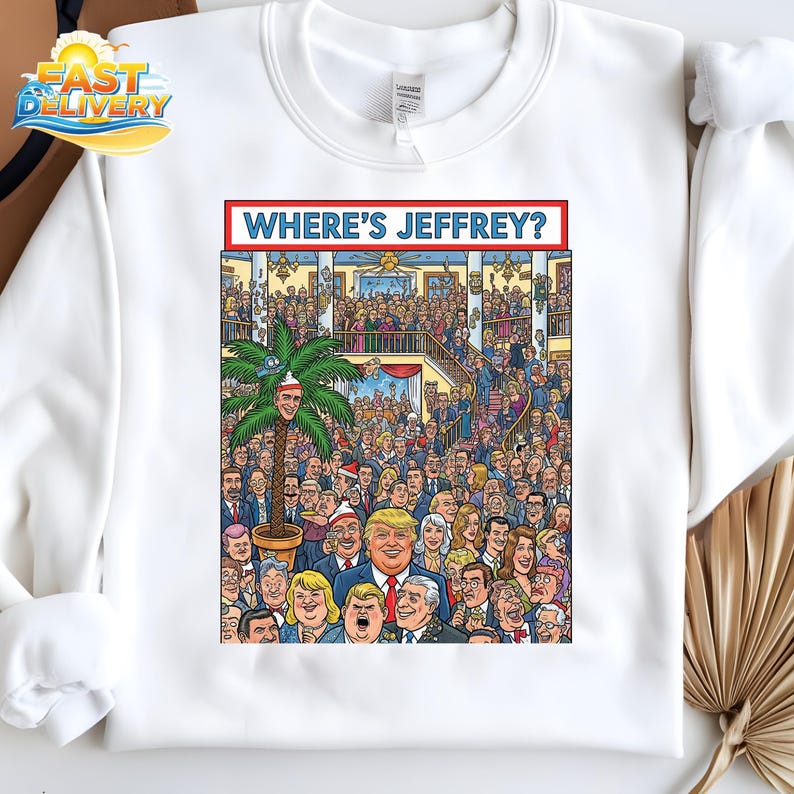 May include: White sweatshirt featuring a colorful cartoon illustration with the text "WHERE'S JEFFREY?" The graphic depicts a large crowd of people, with a palm tree and a man's face in the center.
