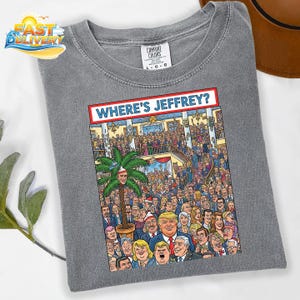 May include: Gray Comfort Colors t-shirt with a colorful graphic. The graphic features a crowd of people and the text "WHERE'S JEFFREY?" in a red and white banner. The shirt is a size L-G-G.