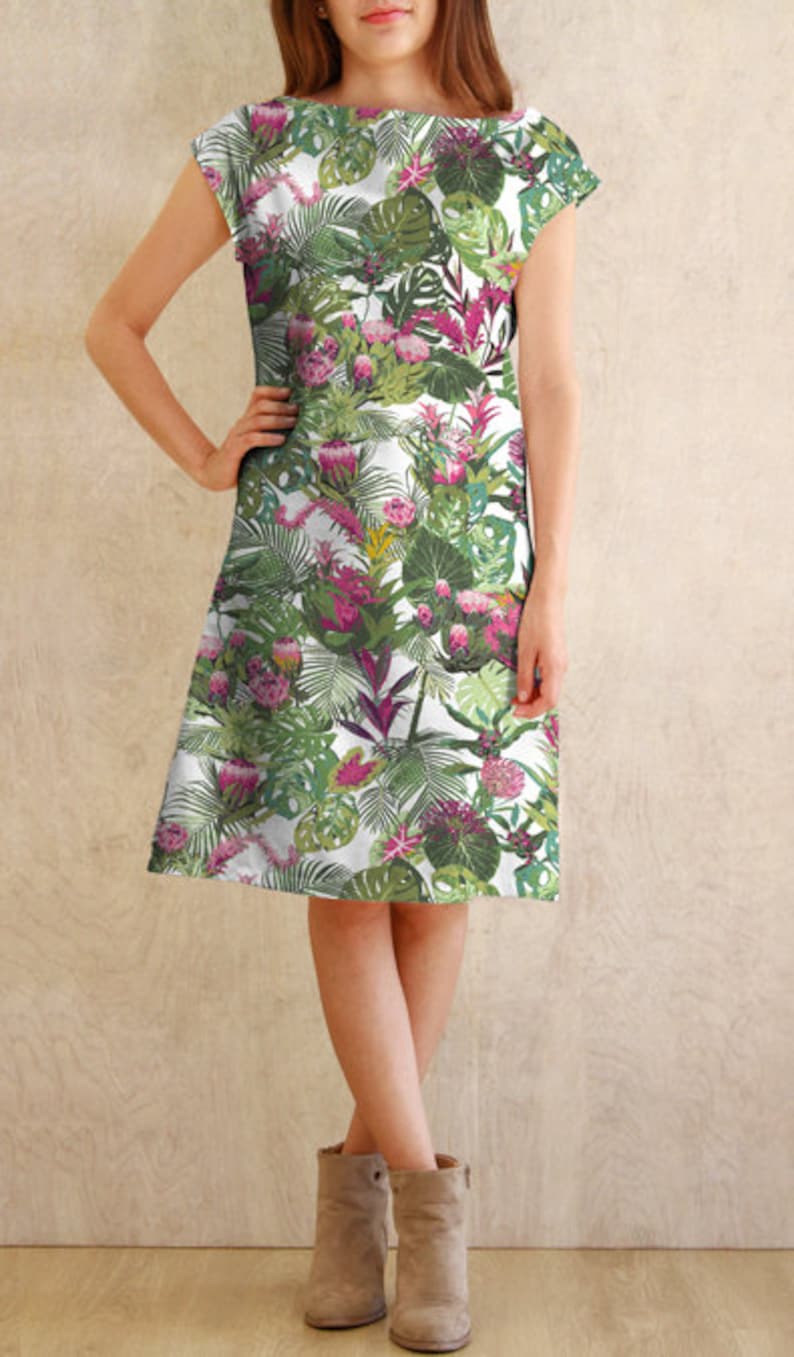 May include: A white dress with a tropical print featuring green leaves, pink flowers, and a white background. The dress has a boat neck and short sleeves.