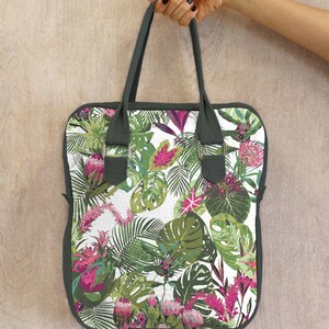 May include: A green tote bag with a white background and a tropical floral print. The print features pink flowers, green leaves, and white accents.