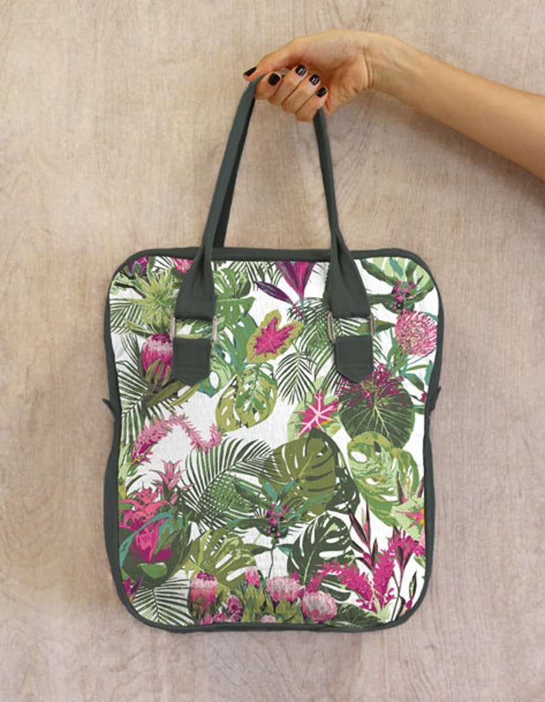 May include: A green tote bag with a white background and a tropical floral print. The print features pink flowers, green leaves, and white accents.