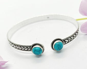 May include: A silver-toned cuff bracelet with two oval turquoise stones. The bracelet has a detailed leaf pattern along the sides and a textured rope design around the turquoise stones. The open design allows for easy wear.