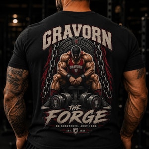 Può includere: Una t-shirt nera con una grafica sul retro raffigurante una figura muscolosa seduta su una panca con manubri. Il testo recita GRAVORN IRON CLUB, THE FORGE, NO SHORTCUTS. JUST IRON. EST. G 2026. Il design include catene e dettagli in rosso.