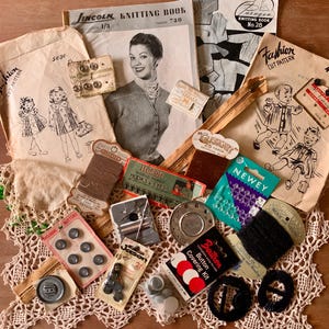 May include: A collection of vintage sewing supplies including Lincoln and Paragon knitting books, paper patterns, metal zips, Newey hooks and eyes, Chadwick wool, button covering kits, assorted buttons, and needles arranged on a lace doily.