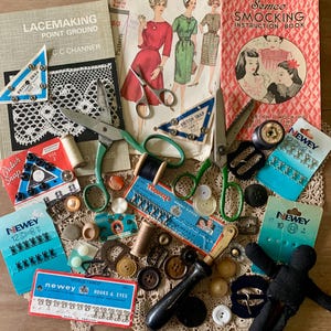 May include: A collection of vintage sewing supplies including two pairs of green-handled scissors, various Newey brand fasteners, hooks and eyes, snap buttons, wooden spools, a tracing wheel, a black fabric doll, and instructional books for lacemaking and smocking.