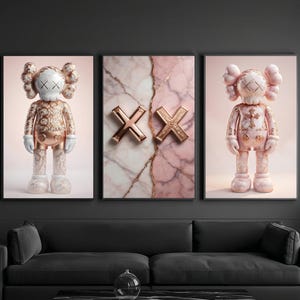 K&ouml;nnte beinhalten: Triptychon-Wandkunst mit einem zentralen Panel mit zwei goldenen "XX" Symbolen auf einem rosa Marmorhintergrund. Seitliche Panels zeigen stilisierte Figuren in Gold- und Rosat&ouml;nen mit wei&szlig;en Akzenten. Das Kunstwerk wird &uuml;ber einem schwarzen Sofa pr&auml;sentiert.