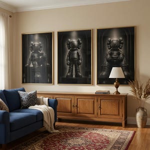May include: Three framed wall art prints featuring black KAWS-style figures with X-shaped eyes. The figures are depicted in different poses against a dark, arched background. Each print is encased in a thin gold frame, displayed in a horizontal row.