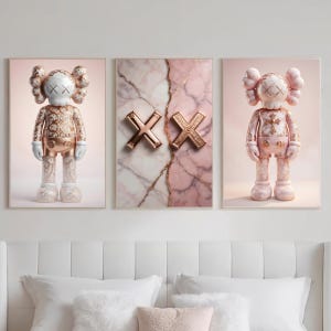 K&ouml;nnte beinhalten: Dreiteiliges Wandkunst-Set. Das zentrale Bild zeigt zwei goldene "XX" Symbole auf rosa Marmorhintergrund. Die seitlichen Paneele zeigen stilisierte Figuren mit kreuzf&ouml;rmigen Augen in Gold und Rosa, f&uuml;r eine harmonische Dekoration.