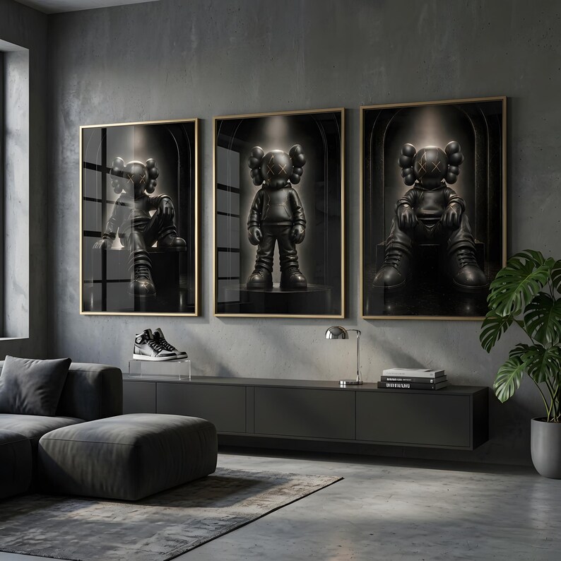 May include: Three framed wall art prints featuring a black character with X-shaped eyes and ears, depicted in different poses within a dark, arched setting. The prints are displayed in thin gold frames on a grey wall above a long black console table.