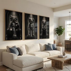 May include: A set of three framed wall art prints featuring a black KAWS-style character figure in different poses. Each print displays the character with X-shaped eyes, wearing a hoodie and sneakers, set against a dark, arched background.