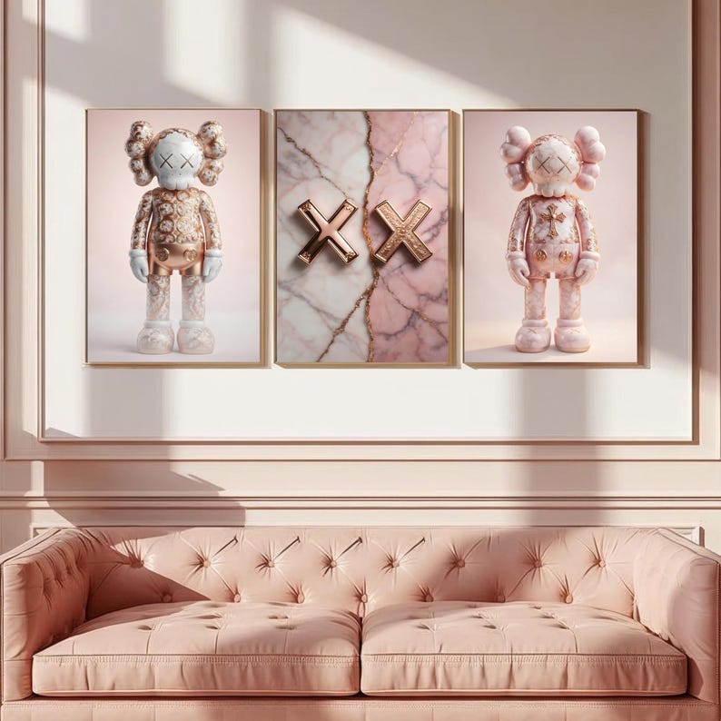 K&ouml;nnte beinhalten: Drei gerahmte Kunstwerke. Zwei zeigen eine cartoonartige Figur mit durchgestrichenen Augen und einem Kreuz auf der Brust. Das dritte St&uuml;ck hat ein Marmormuster mit goldfarbenen "XX"-Symbolen. Das Farbschema ist haupts&auml;chlich rosa und gold.