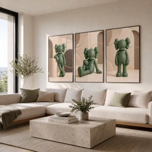 May include: A set of three framed wall art prints featuring a matte olive green cartoon character with X-shaped eyes. Each print displays the character in a different pose against a neutral beige background with abstract geometric shapes and arches.