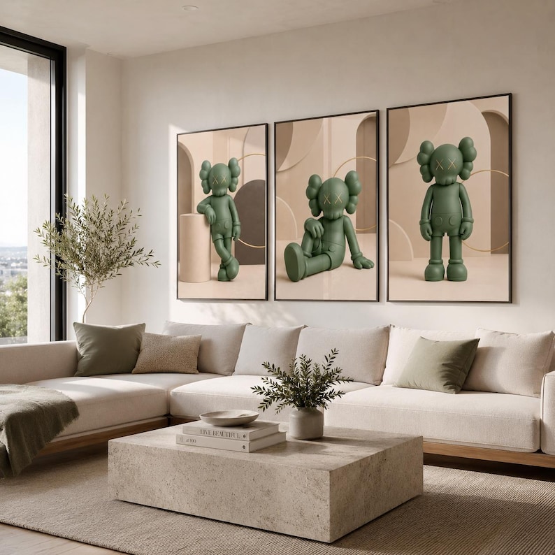 May include: A set of three framed wall art prints featuring a matte olive green cartoon character with X-shaped eyes. Each print displays the character in a different pose against a neutral beige background with abstract geometric shapes and arches.
