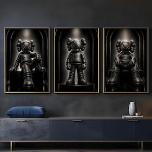 May include: A set of three framed wall art prints featuring black cartoon-style figures with X-shaped eyes. Each figure wears a hooded sweatshirt and trainers, positioned within a dark, arched alcove setting with subtle gold-toned accents.