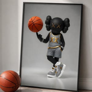 May include: Framed artwork featuring a black figure with crossed-out eyes, wearing a gray basketball uniform with gold accents, balancing an orange basketball on a finger. A second basketball rests on the floor.