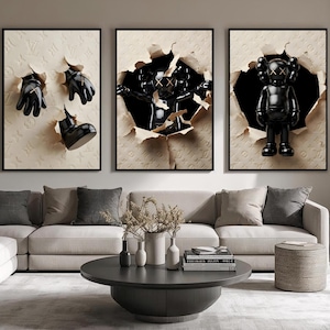 Puede incluir: Tres obras de arte enmarcadas con figuras y objetos negros que emergen de papel rasgado. El arte incluye una figura negra con ojos tachados, guantes negros y una bota negra. El fondo es un patr&oacute;n en relieve beige.