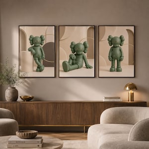 May include: A set of three framed wall art prints featuring a matte olive green cartoon character with X-shaped eyes. Each print displays the character in a different pose against a neutral beige background with abstract geometric shapes and arches.