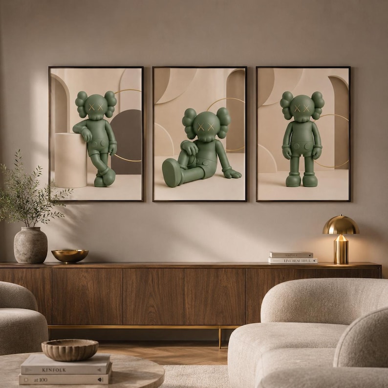 May include: A set of three framed wall art prints featuring a matte olive green cartoon character with X-shaped eyes. Each print displays the character in a different pose against a neutral beige background with abstract geometric shapes and arches.