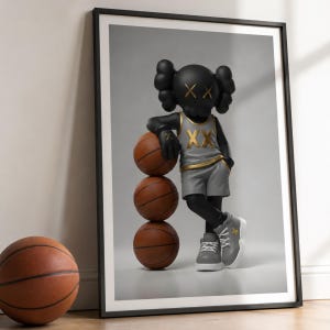 May include: Framed art print featuring a black figure with crossed-out eyes, wearing a gray basketball uniform, leaning on three basketballs. The figure's pose is casual, with one leg crossed. The basketballs are brown.