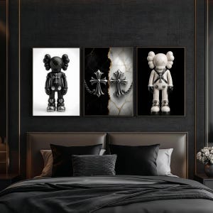 May include: Three framed art pieces featuring a black and white color scheme. One shows a black figure with silver accents, another has two silver crosses on a marble background, and the last displays a white figure with black accents. The art is displayed above a bed.