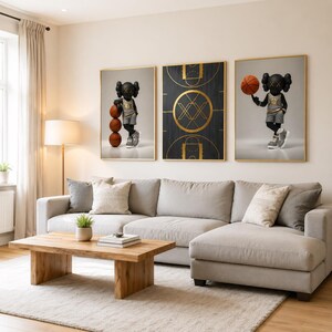 May include: Three framed art prints featuring a basketball theme. Two prints depict a black figure with a basketball, and the center print shows a gold and black basketball court design. The prints are displayed above a light gray sectional sofa.