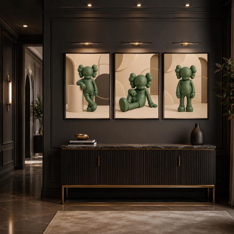 May include: A set of three framed wall art prints featuring a green cartoon character with X-shaped eyes in different poses. The character is depicted against a neutral beige background with geometric shapes, displayed above a dark sideboard.