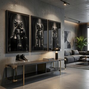 May include: Three framed wall art prints featuring black stylised figures with cross-shaped eyes, displayed above a long black and gold console table. The table holds a pair of black high-top trainers, a stack of books, and a black table lamp.