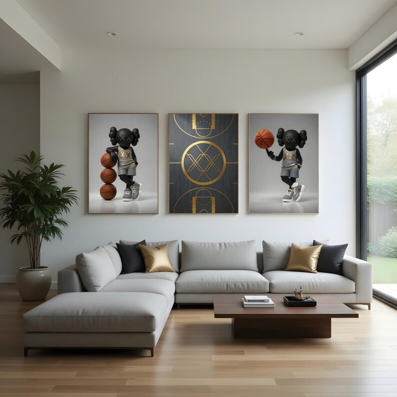 May include: Three framed art prints displayed on a white wall. The prints feature a black figure with basketballs, a basketball court design, and a figure holding a basketball. The room has a gray sectional sofa, a wooden coffee table, and a large window.