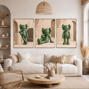 May include: A set of three framed wall art prints featuring a green cartoon character with X-shaped eyes. The first print shows the character leaning on a cylinder, the second shows it sitting, and the third shows it standing in a neutral room.