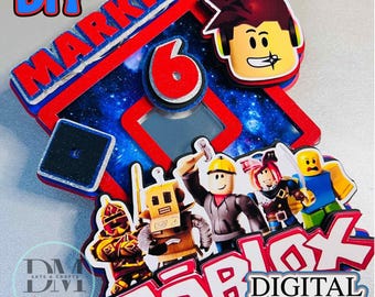 May include: A colorful Roblox-themed cake topper with the name "Markie" and the number "6" in red. The design includes Roblox characters and the text "DIGITAL FILE". The background features a starry sky.
