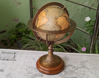 May include: A vintage-style globe with a brass frame and a wooden base. The globe features a detailed map with tan and gold tones. The brass frame has engraved markings. The globe is a decorative item.