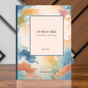 Peut inclure: Un livre à couverture rigide avec un design abstrait coloré dans les tons de bleu, orange et rose. La couverture porte le texte "So You'll Know" et "50 Guided Questions to Share Your Story" avec l'année "Since 1976".