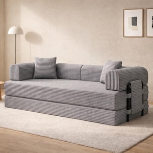 May include: A gray corduroy sofa with two matching throw pillows. The sofa has a low profile and a modular design, with a section that can be folded up. The sofa is on a light-colored rug.